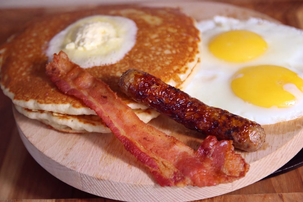Pancakes with butter, two sunny-side-up eggs, bacon and a sausage link