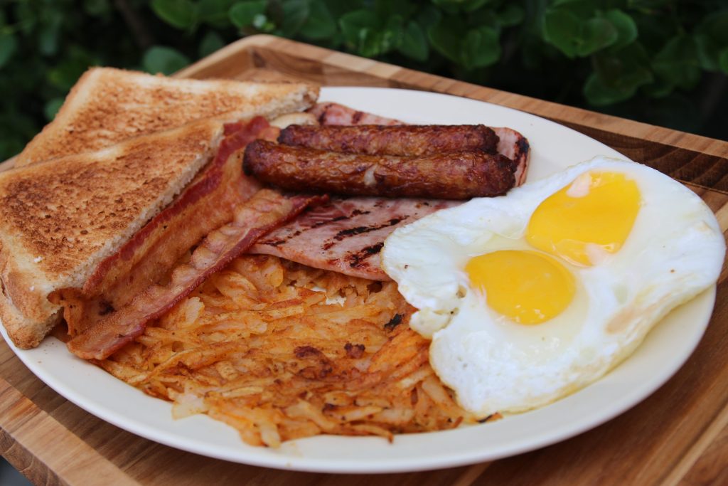 Breakfast plate with two eggs, hash browns, bacon, ham, sausage and toast